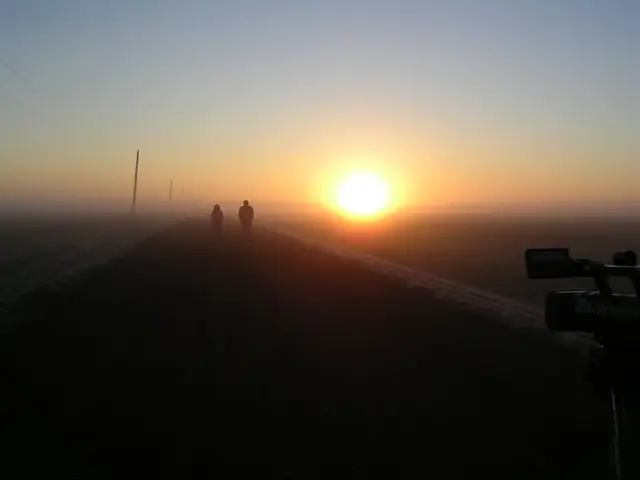 Sunrise over a foggy prairie road with two people and a video camera